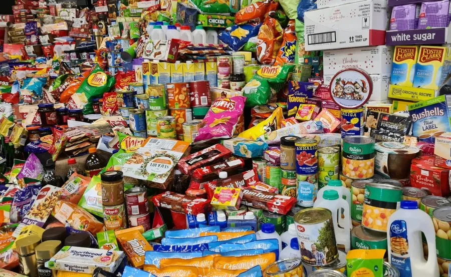 A chaotic pile of ultra-processed food packages, cans, and snacks